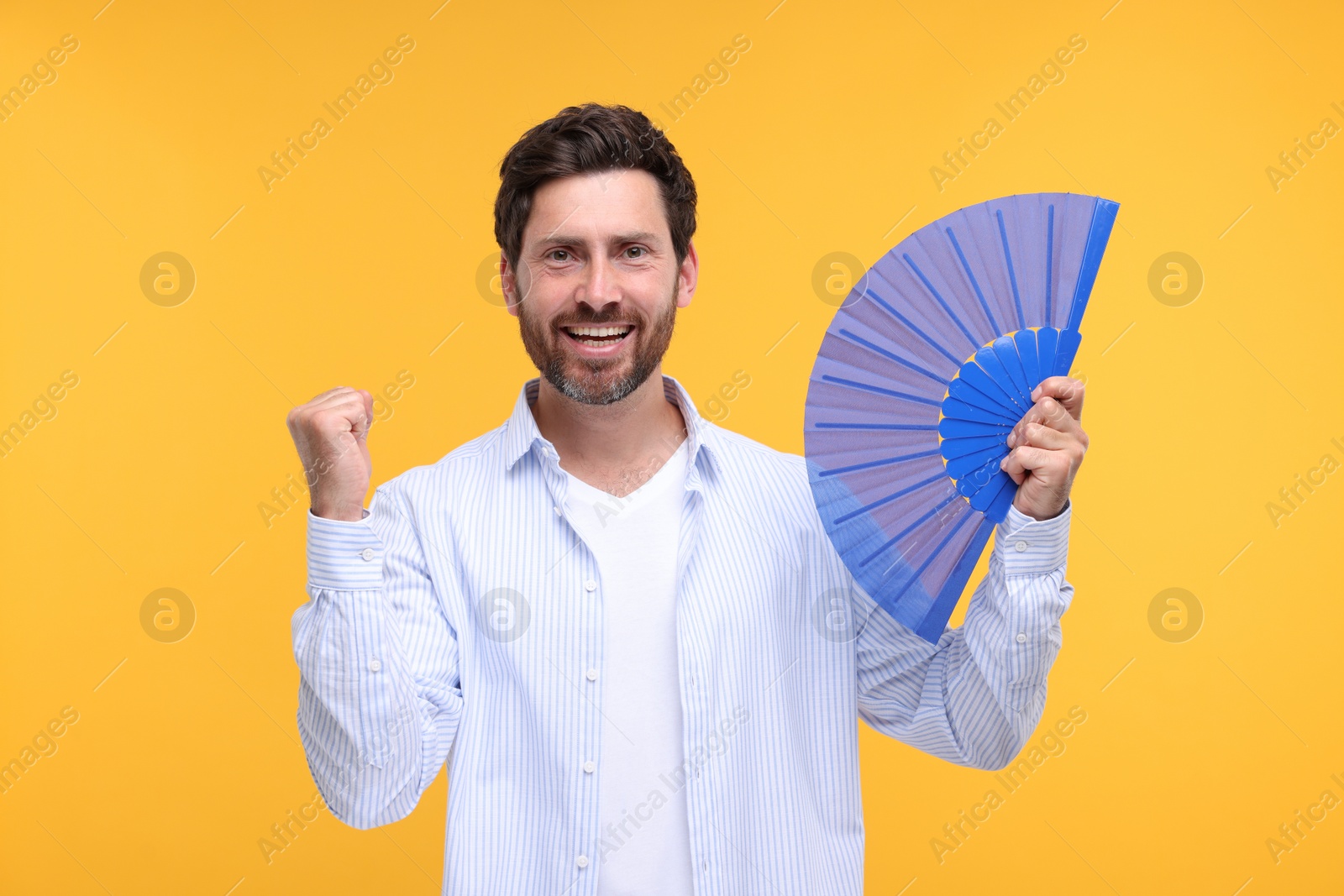 Photo of Happy man holding hand fan on orange background