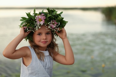 Photo of Cute little girl wearing wreath made of beautiful flowers near river