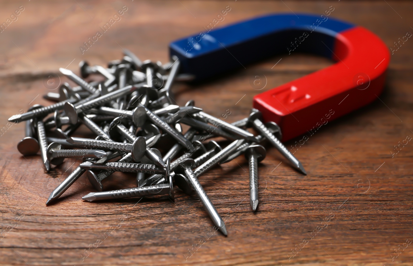 Photo of Magnet attracting nails on wooden background, closeup