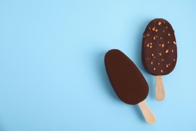 Photo of Ice cream bars glazed in chocolate on light blue background, flat lay. Space for text