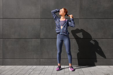 Photo of Beautiful woman in stylish gym clothes near dark grey wall on street, space for text
