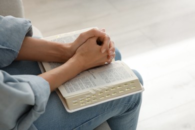 Religious woman with Bible praying indoors, closeup