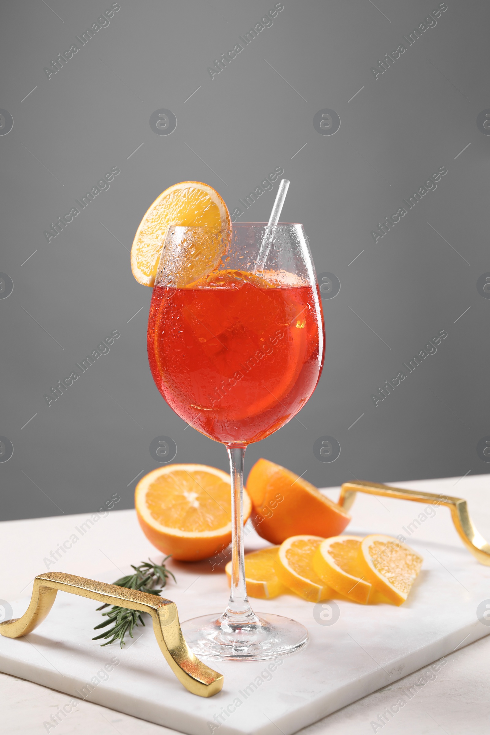 Photo of Glass of tasty Aperol spritz cocktail with orange slices and rosemary on white table against gray background