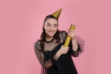 Photo of Young woman blowing up party popper on pink background
