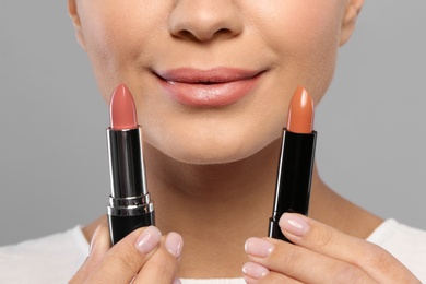Photo of Young woman with lipsticks on gray background, closeup