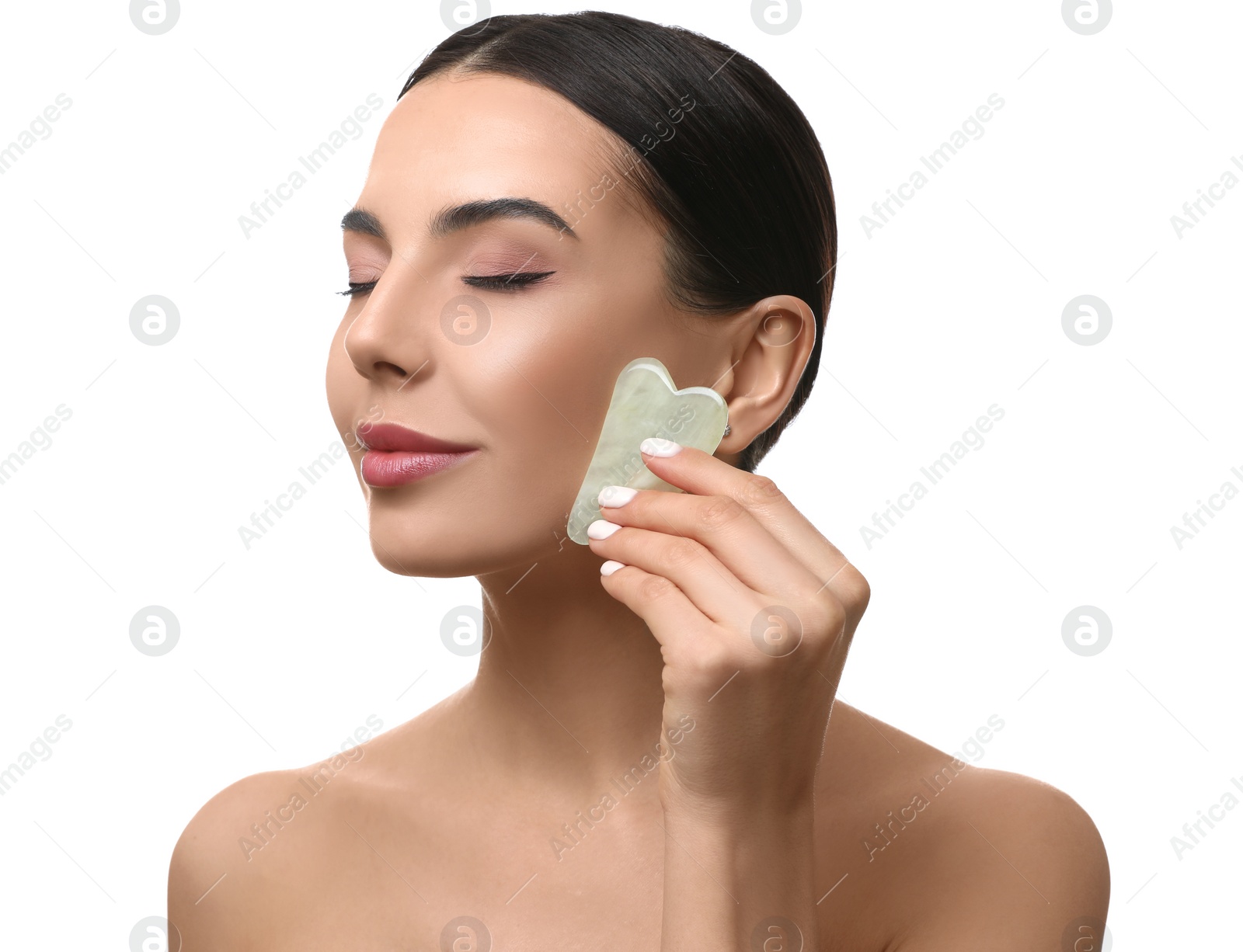 Photo of Beautiful young woman doing facial massage with gua sha tool on white background