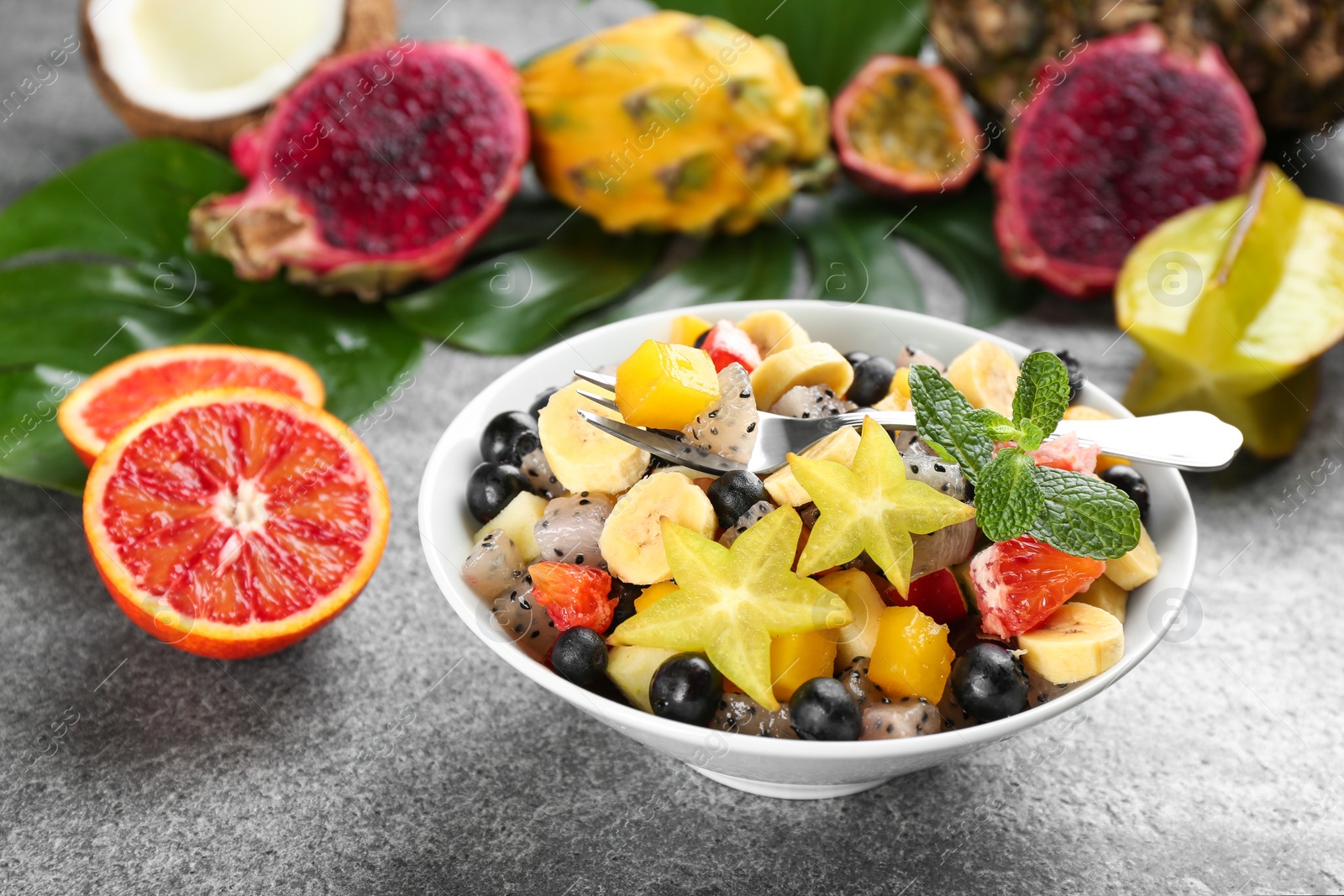 Photo of Delicious exotic fruit salad and ingredients on grey table