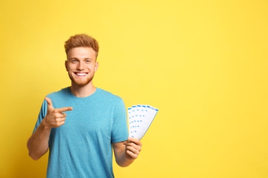 Photo of Portrait of happy young man with lottery tickets on yellow background