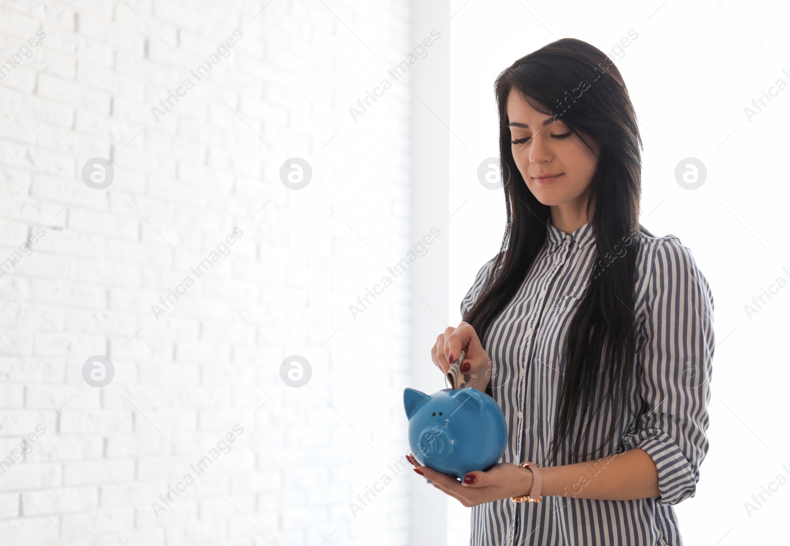 Photo of Woman putting money into piggy bank indoors, space for text