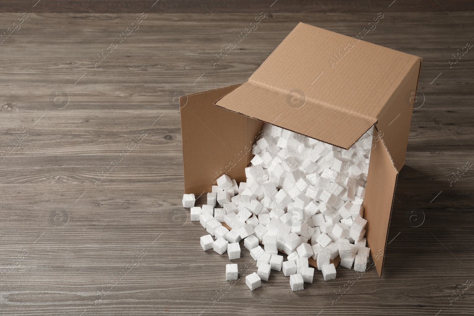 Photo of Overturned cardboard box with styrofoam cubes on wooden floor. Space for text