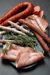 Photo of Different tasty sausages and rosemary on black table