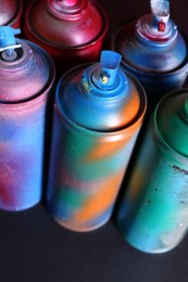 Photo of Many spray paint cans on black background, above view