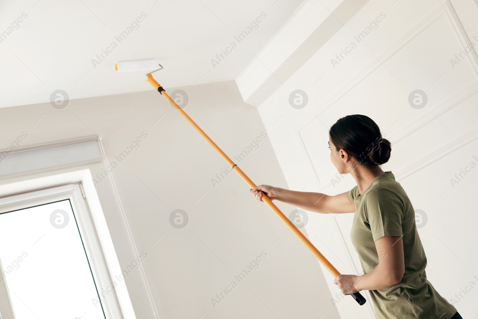 Photo of Young woman painting ceiling with white dye indoors, space for text