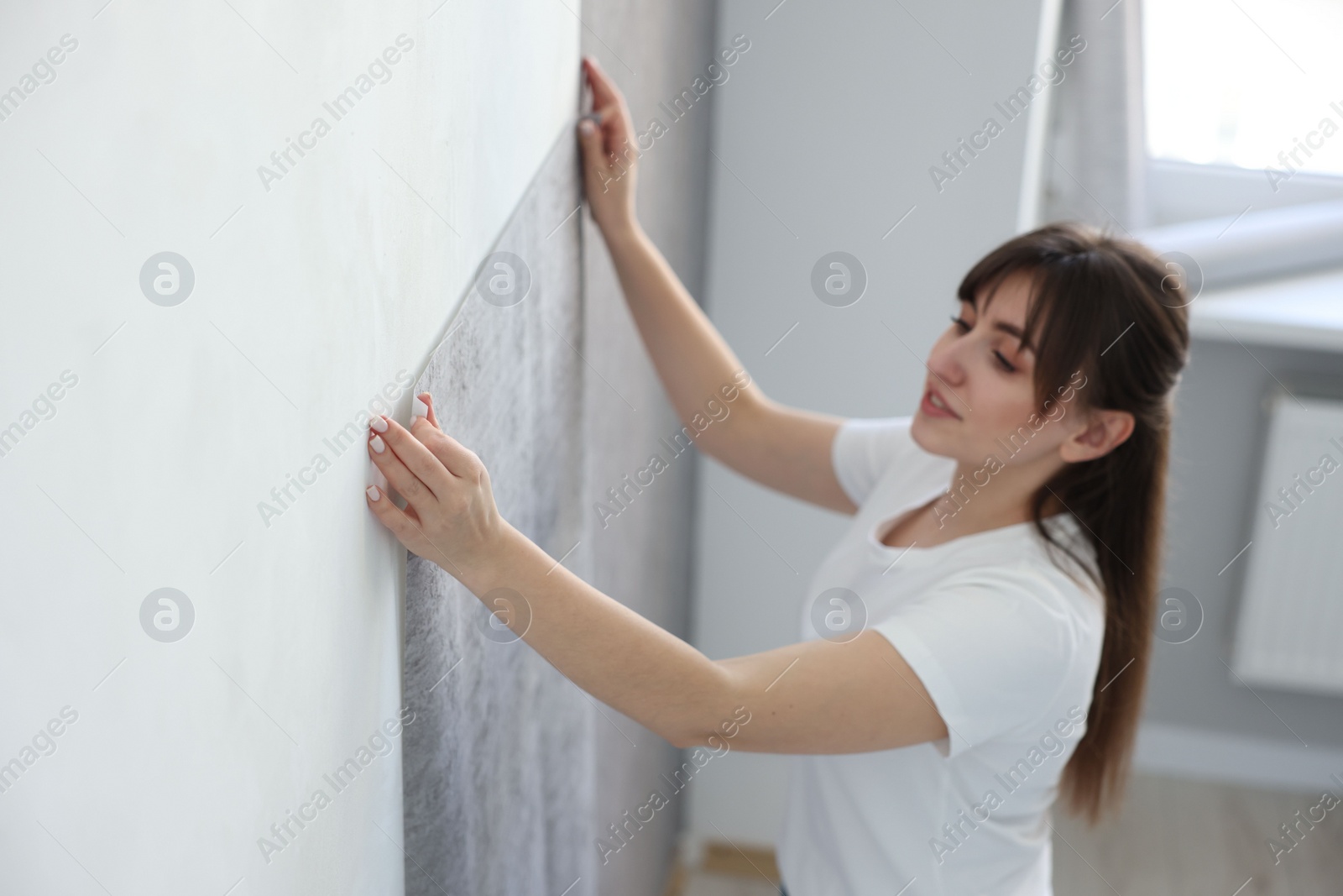 Photo of Woman hanging stylish gray wallpaper in room