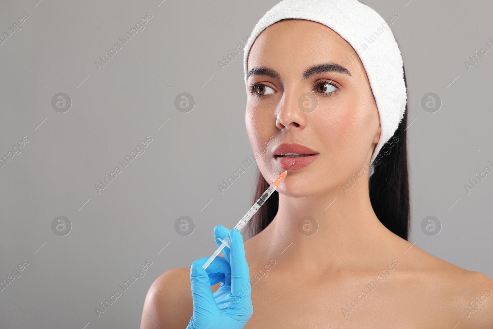 Photo of Doctor giving lips injection to young woman on light grey background, space for text. Cosmetic surgery