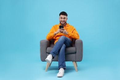 Photo of Happy young man using smartphone on armchair against light blue background