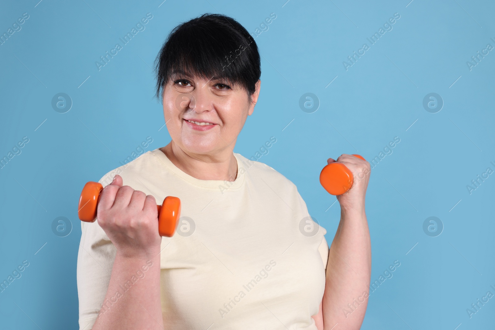 Photo of Happy overweight mature woman doing exercise with dumbbells on light blue background