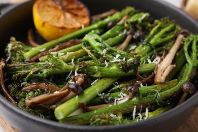 Photo of Tasty cooked broccolini, mushrooms and lemon in serving pan, closeup
