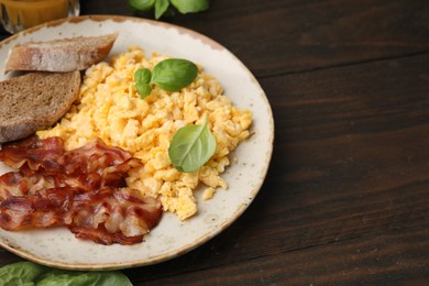 Photo of Delicious scrambled eggs with bacon and products on wooden table. Space for text