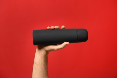 Photo of Man holding black thermos on red background, closeup