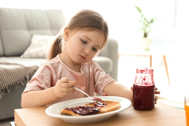 Little girl spreading jam on toast in living room