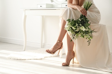 Photo of Young bride wearing wedding dress with beautiful bouquet in room, closeup. Space for text