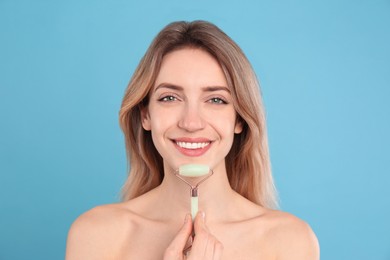 Young woman using natural jade face roller on light blue background