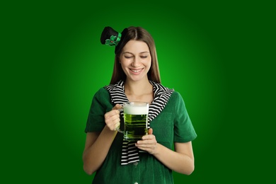 Happy woman in St. Patrick's Day outfit with beer on green background