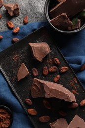 Photo of Pieces of tasty milk chocolate, cocoa beans and powder on grey table, top view