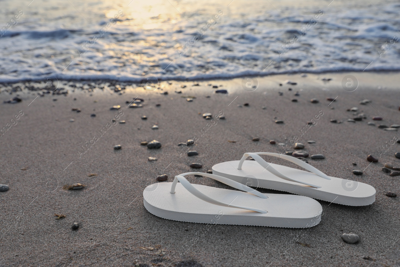 Photo of Stylish white flip flops on sand near sea. Space for text