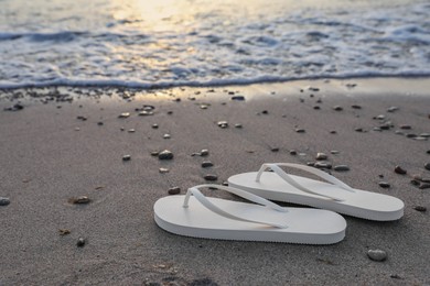 Photo of Stylish white flip flops on sand near sea. Space for text