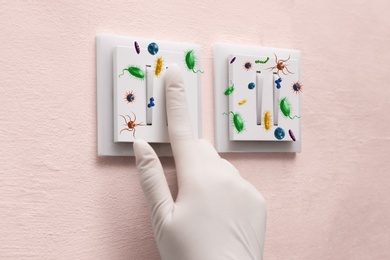 Woman in protective gloves pressing light switch button full of microbes indoors, closeup