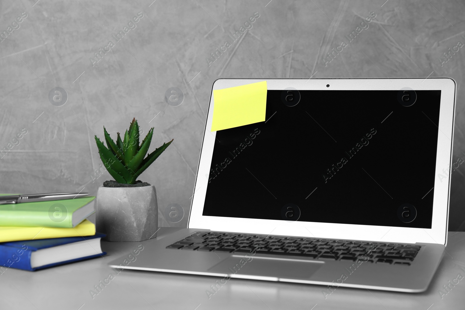Photo of Laptop with empty sticky note and stationery on white table near grey wall. Space for text