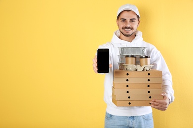 Young man holding orders and smartphone on color background, mockup for design. Online food delivery