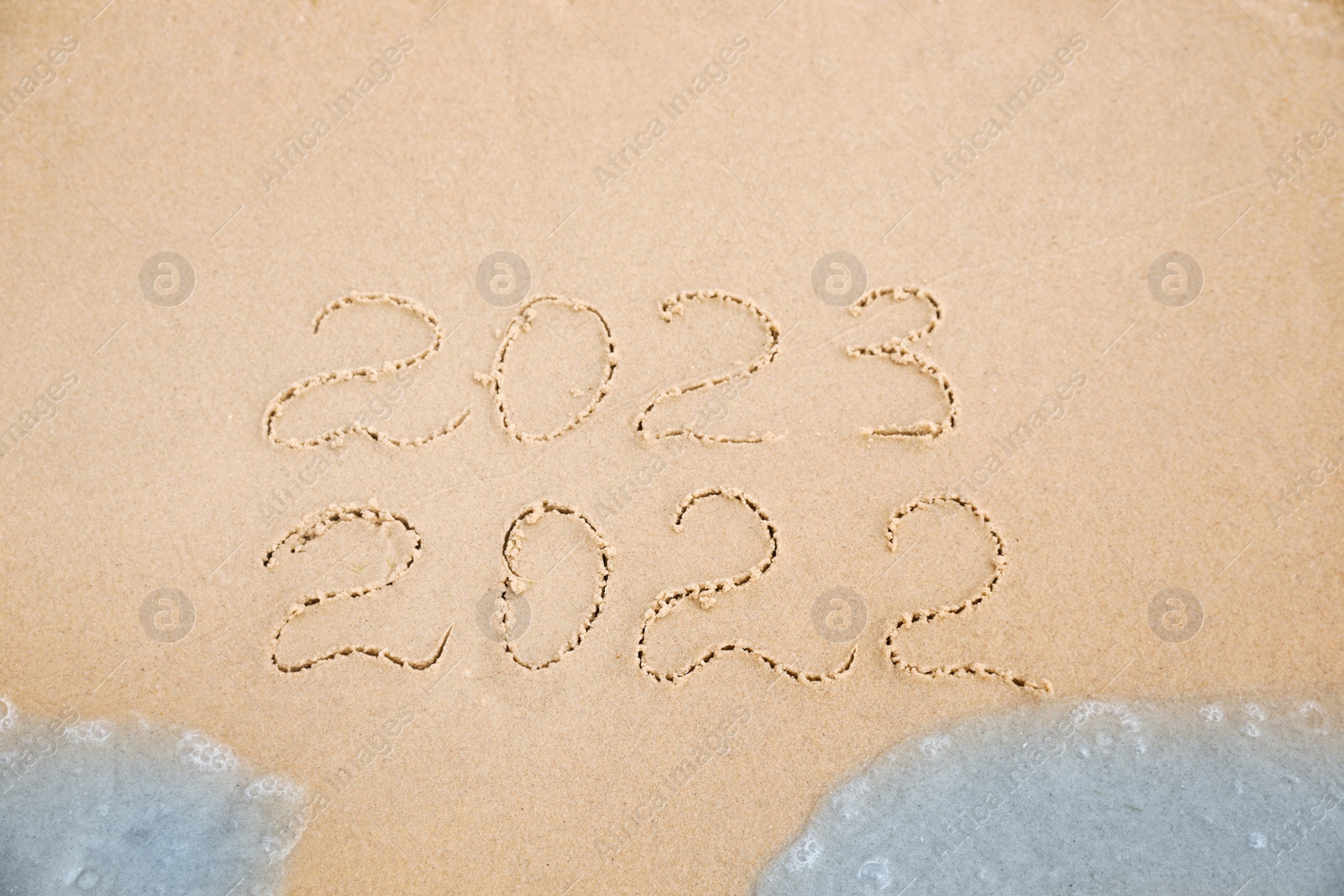 Photo of Dates written on sandy beach. 2022 washed by sea wave as New 2023 Year coming, above view