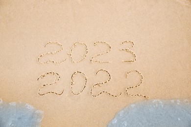 Dates written on sandy beach. 2022 washed by sea wave as New 2023 Year coming, above view