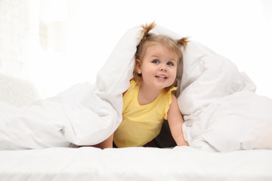 Photo of Cute little child playing under blanket in bed