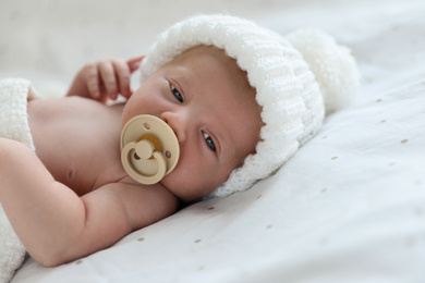 Cute newborn baby in white knitted hat lying on bed
