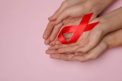 Photo of Woman and girl holding red ribbon on pink background, top view with space for text. AIDS disease awareness