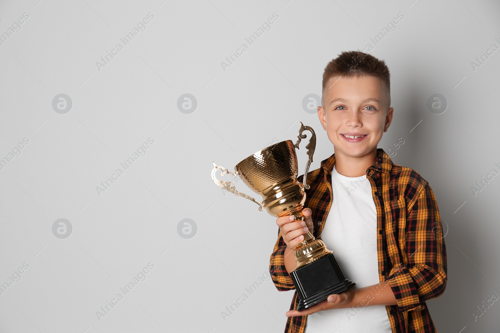 Photo of Happy boy with golden winning cup on light background. Space for text