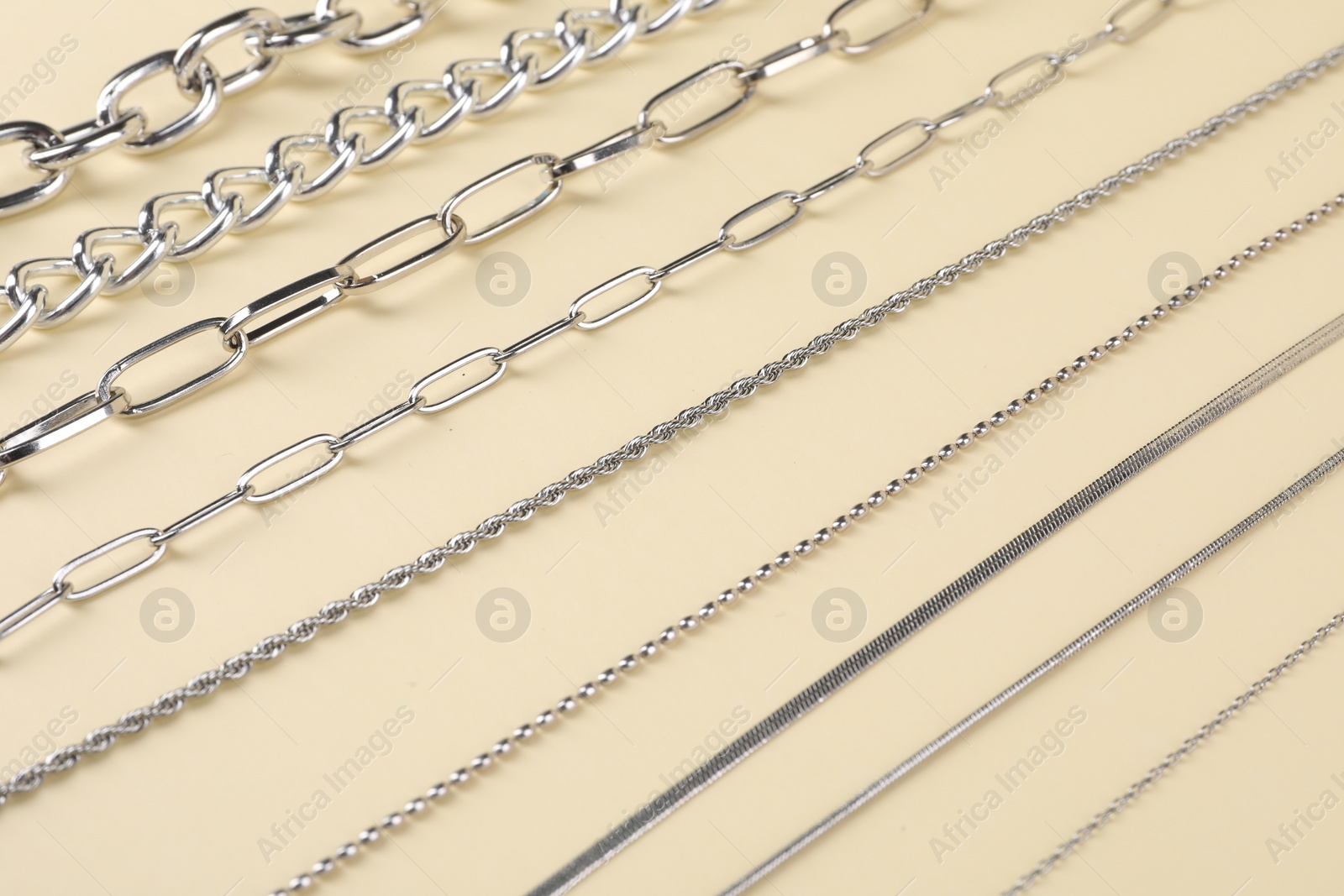 Photo of Different metal chains on beige background, closeup. Luxury jewelry
