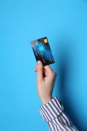 Woman holding credit card on light blue background, closeup