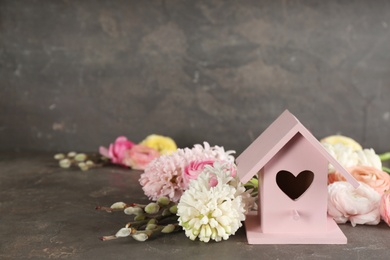 Stylish bird house and fresh flowers on grey stone background. Space for text