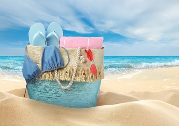 Image of Stylish bag with different accessories on sandy beach near ocean