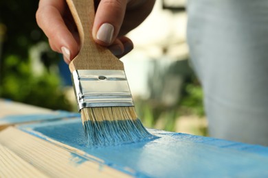 Photo of Woman painting wooden surface with blue dye outdoors, closeup
