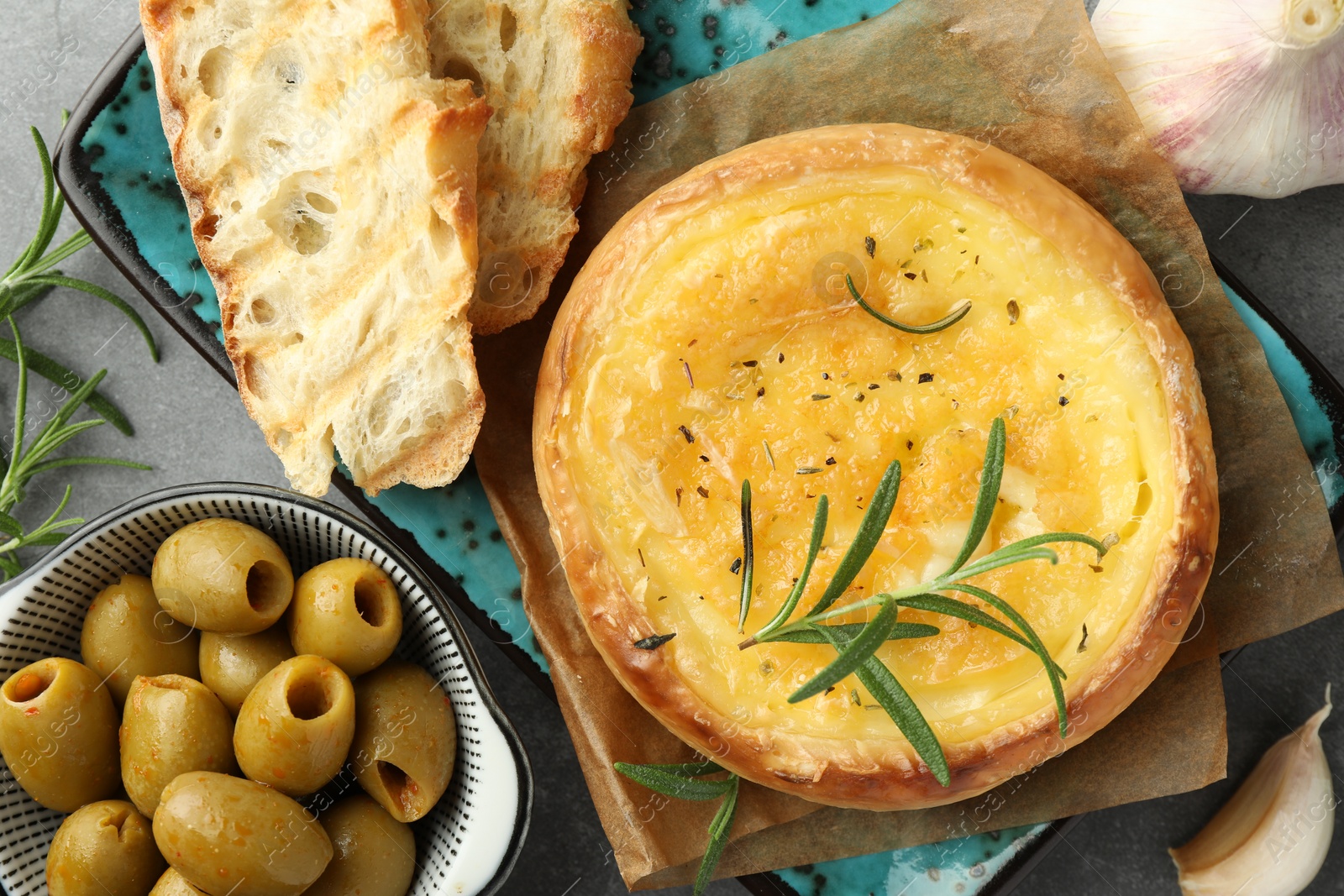 Photo of Tasty baked brie cheese and products on grey table, flat lay