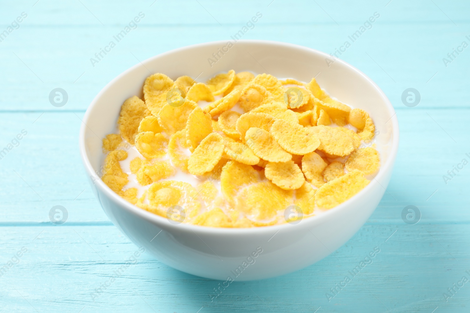 Photo of Tasty crispy corn flakes with milk on light blue wooden  table