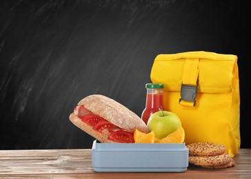 Image of Lunch box with appetizing food and bag on table near black chalkboard, space for text
