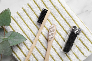Bamboo toothbrushes, natural dental floss, towel and eucalyptus branch on white marble table, flat lay