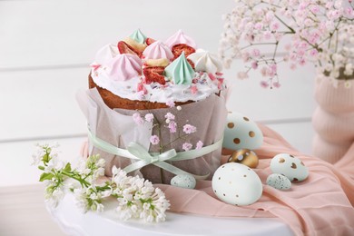 Photo of Traditional Easter cake with meringues and painted eggs on stand near white wooden wall